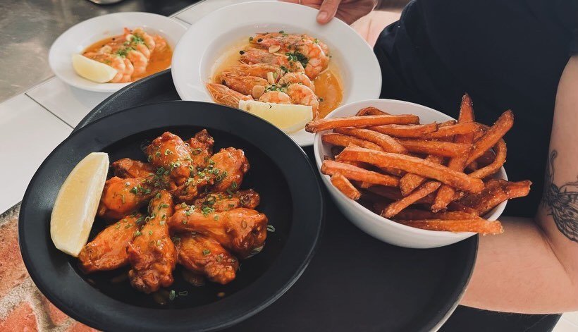 Asas de frango com limão, camarões em molho e batata-doce frita, numa bandeja