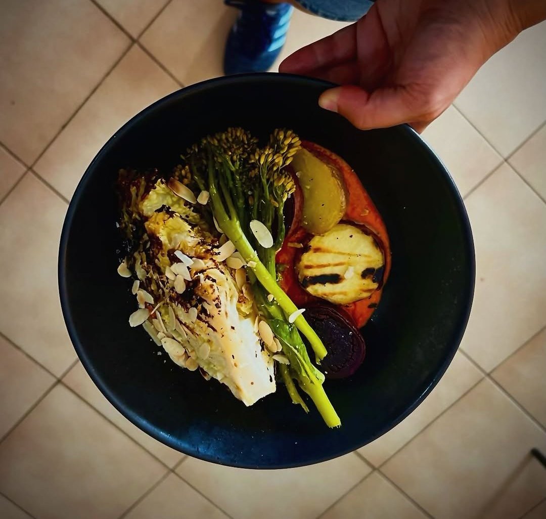 Prato escuro com couve tostada, broccolini, batata roxa e molho